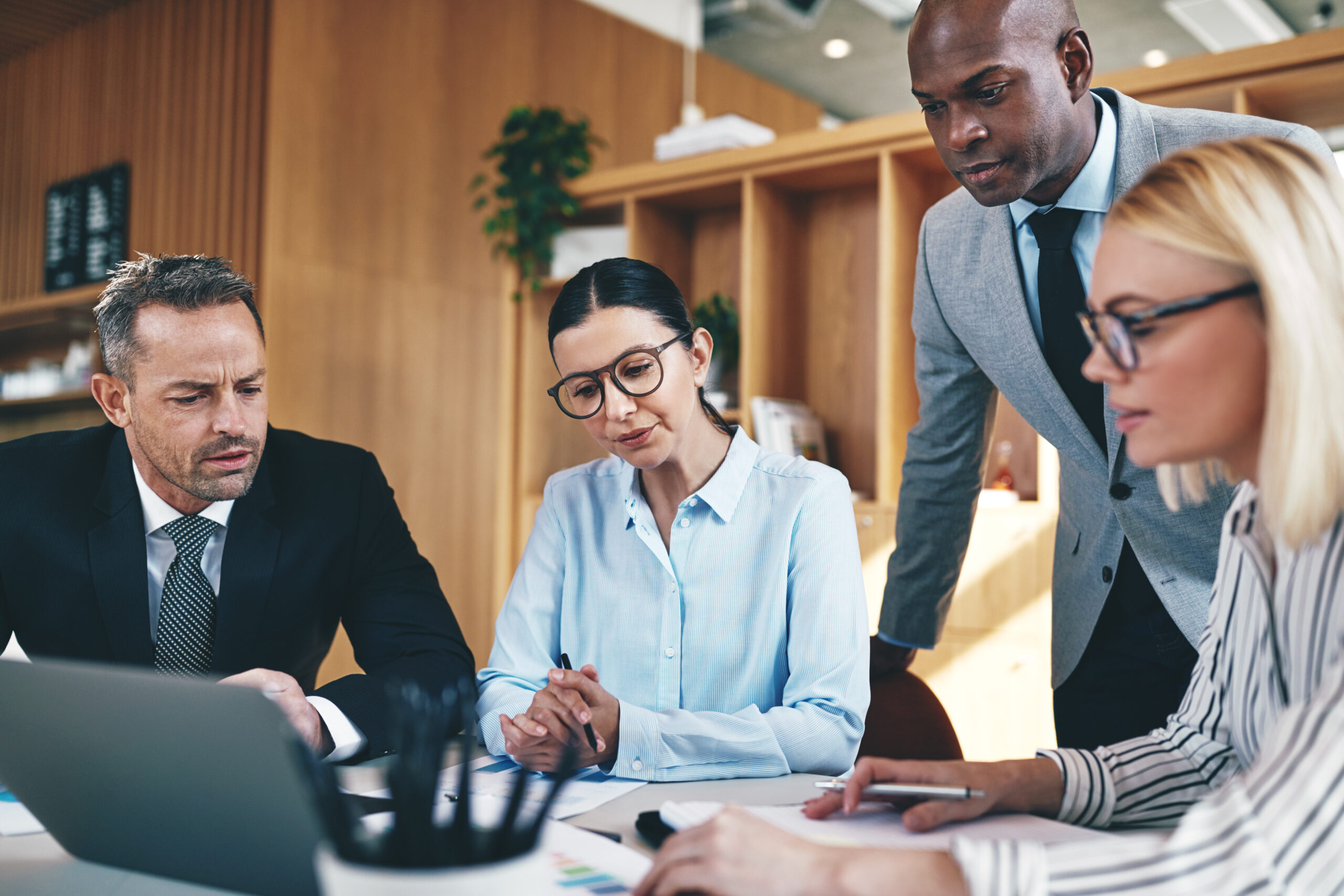 Three business professionals in a meeting room, focused on a laptop during a collaborative discussion.
