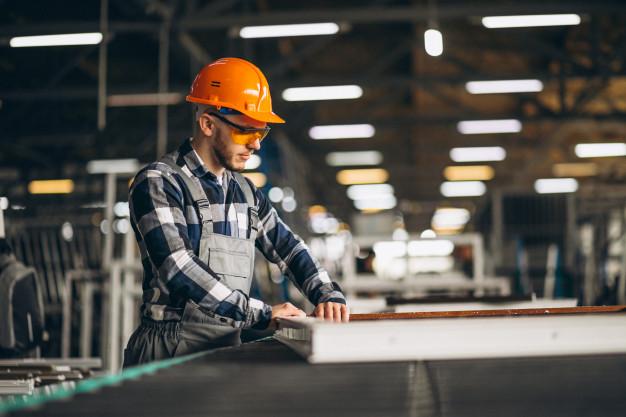 A man wearing a hard hat and safety glasses operates machinery on a production line, highlighting workplace safety.