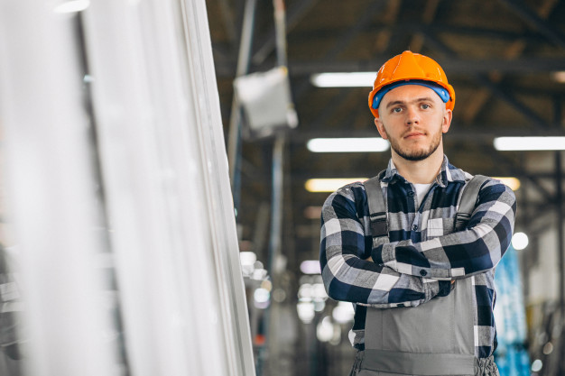 A man wearing a hard hat and overalls stands by a window, highlighting the importance of safety in the construction industry.