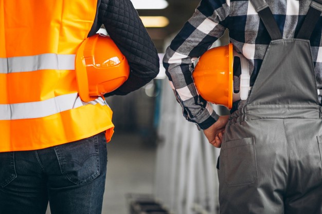 Two construction workers in bright orange safety vests focus on their tasks, showcasing the importance of safety in construction.